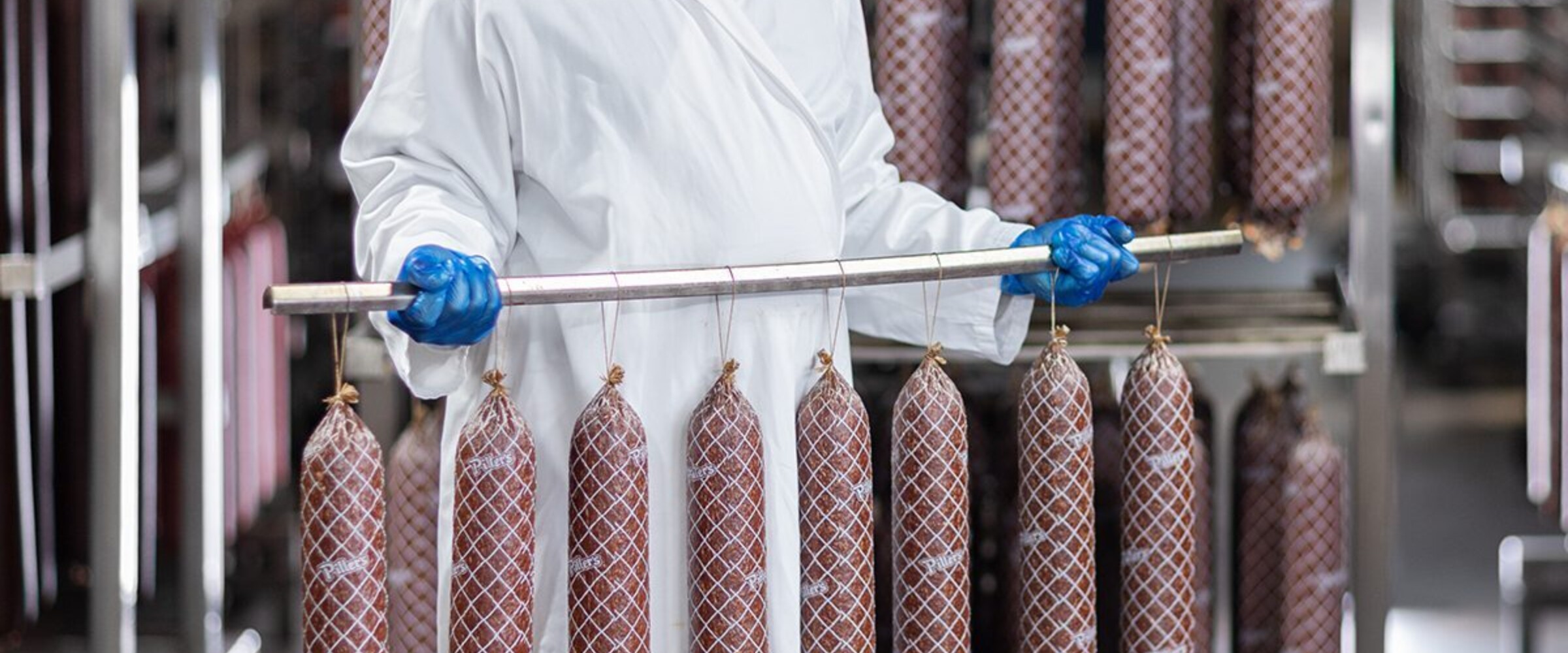 Employee holding rack of drying salami