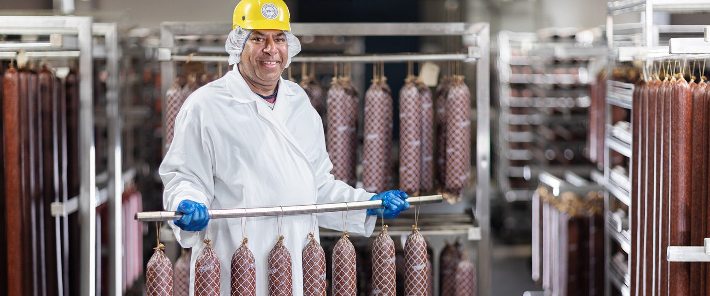 Employee holding rack of drying salami