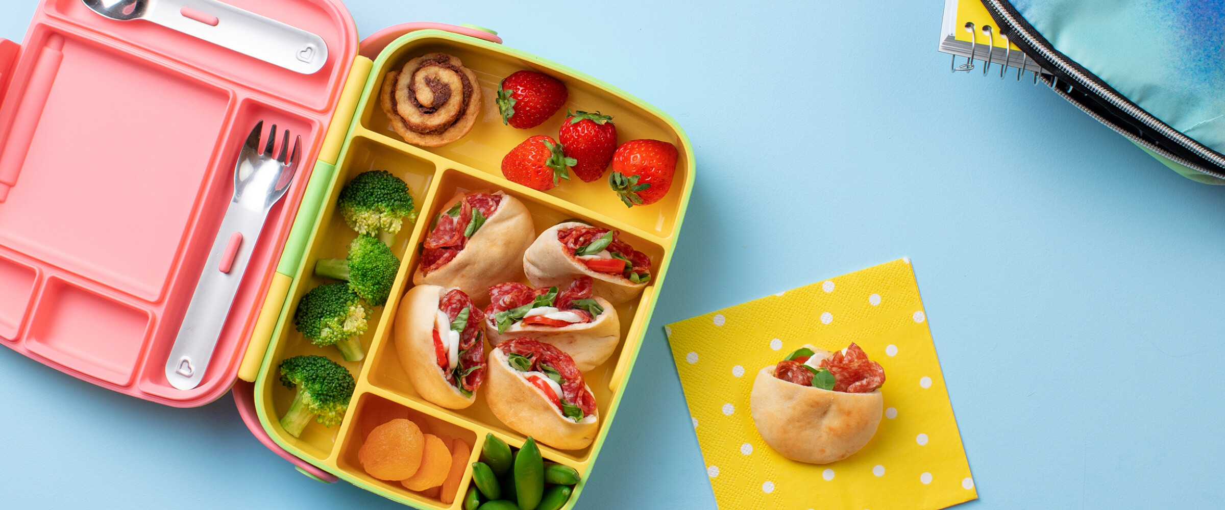 lunch box with pita pizzas with salami, fruits, veggies.
