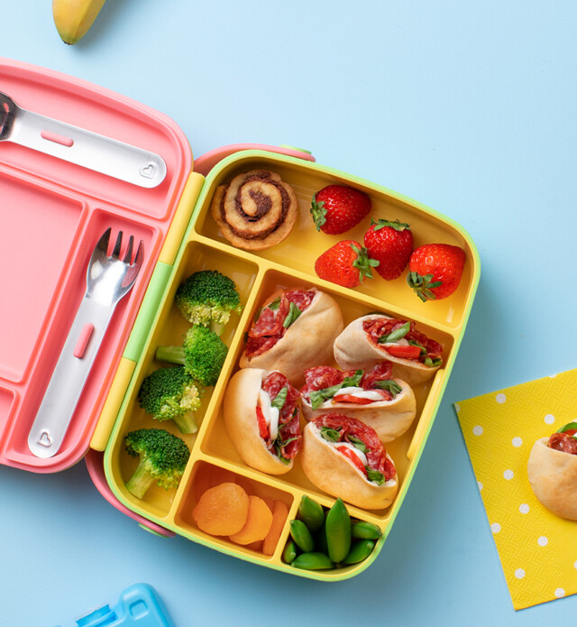 lunch box with pita pizzas with salami, fruits, veggies.
