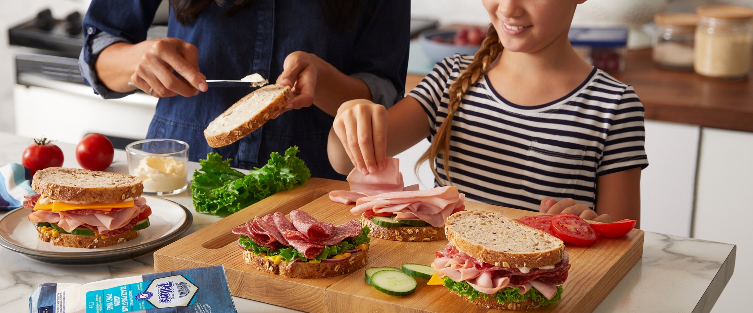 Mother and daughter making sandwiches on wooden cutting board.