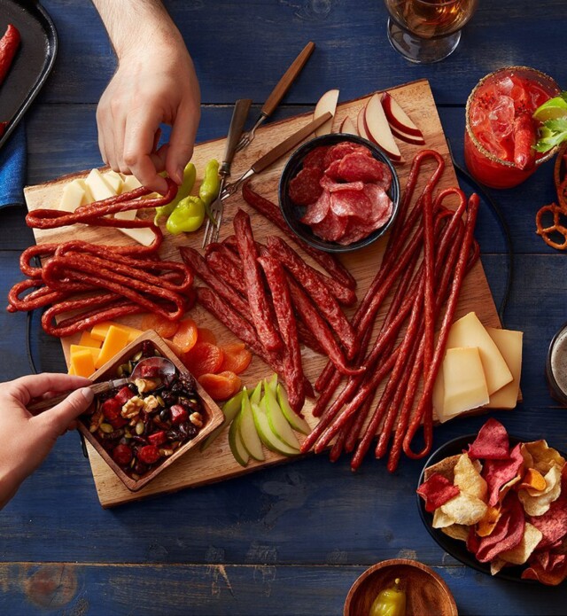 Hands reaching for meat snacks on a board