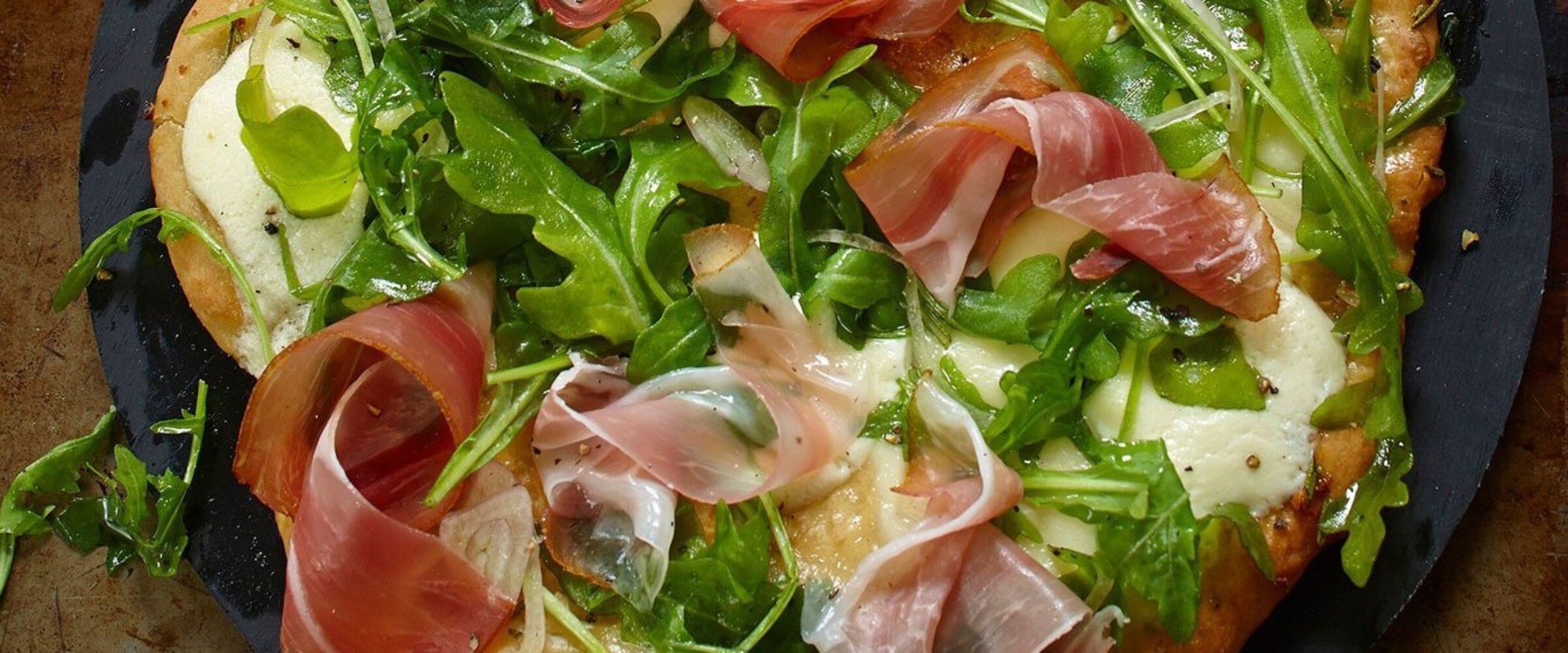 Pizza with arugula and speck prosciutto on a black pan