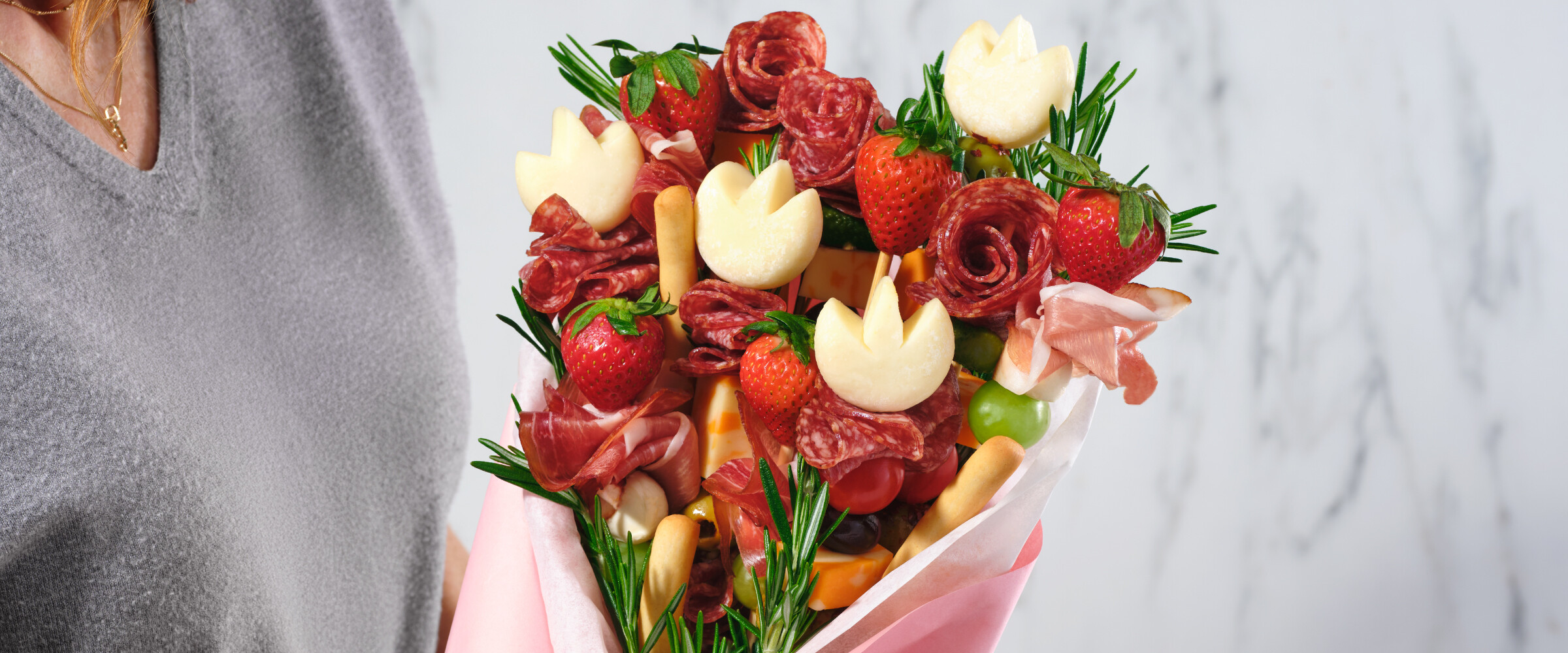 A mix of cheeses, sliced meats and fruits together making a charcuterie bouquet.
