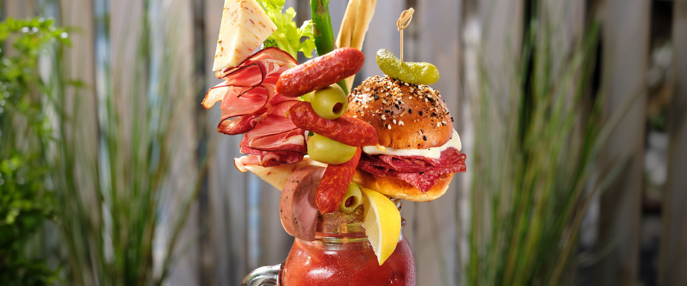 Caesar drink in a mason jar garnished with various veggies and meats.