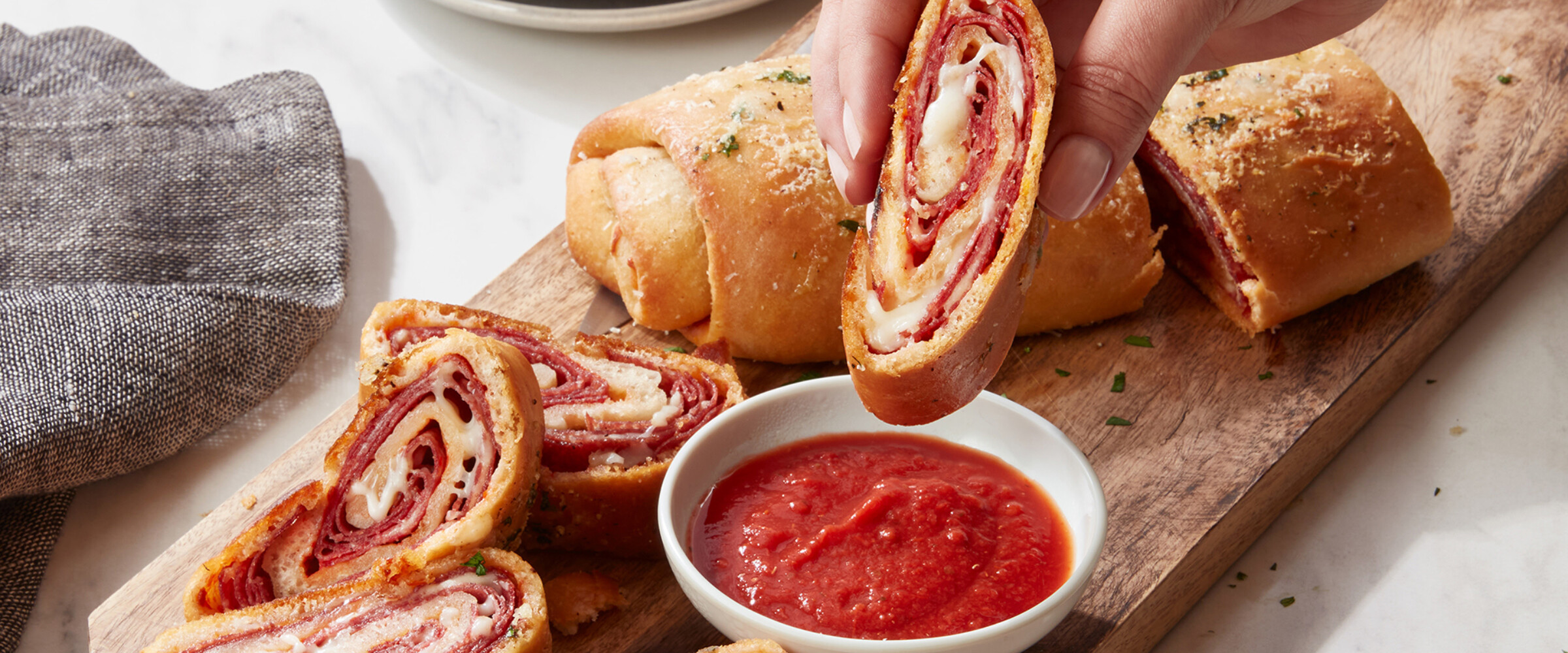 Hand dipping Stromboli into marinara sauce on a wood board