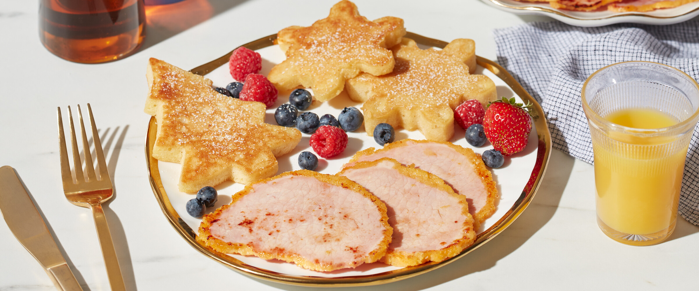 Snowflake and tree shaped pancakes served with berries and peameal bacon on a plate