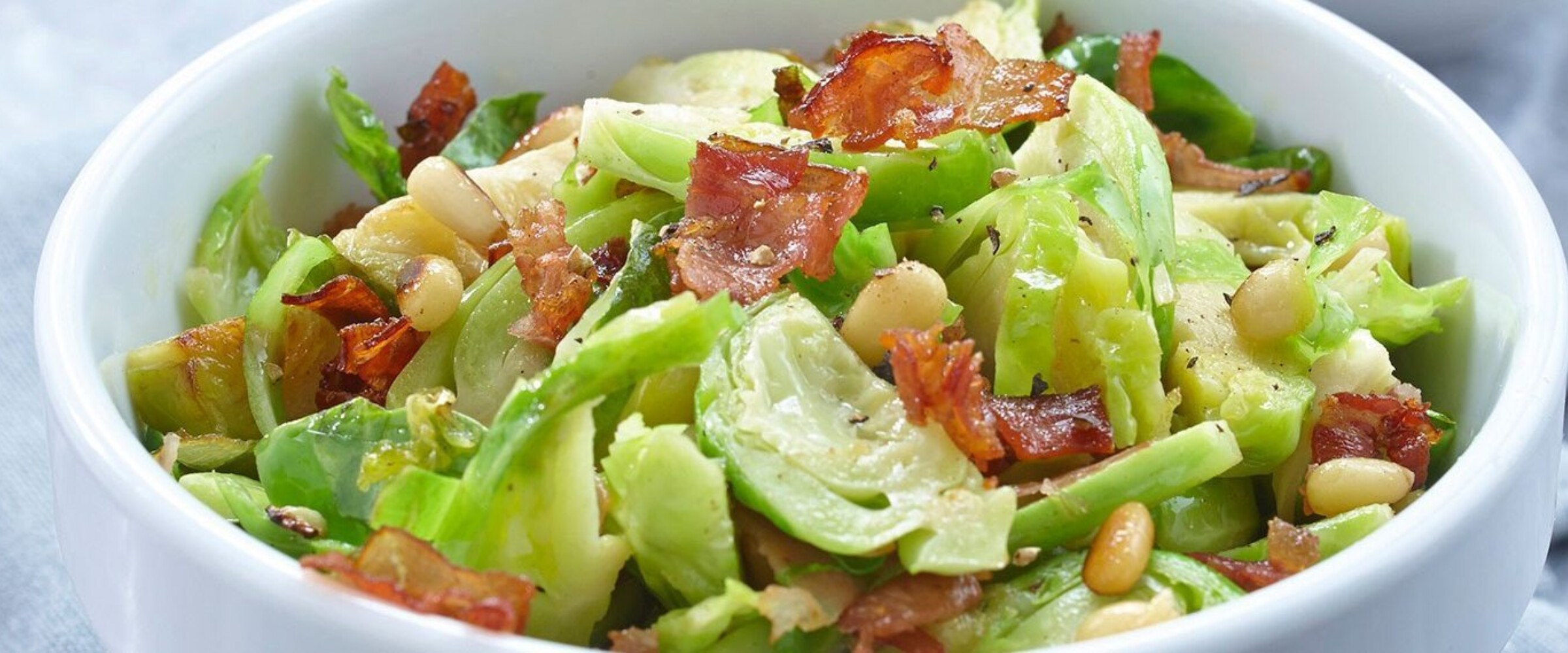 Brussel Sprouts shredded with Speck Prosciutto in a white bowl