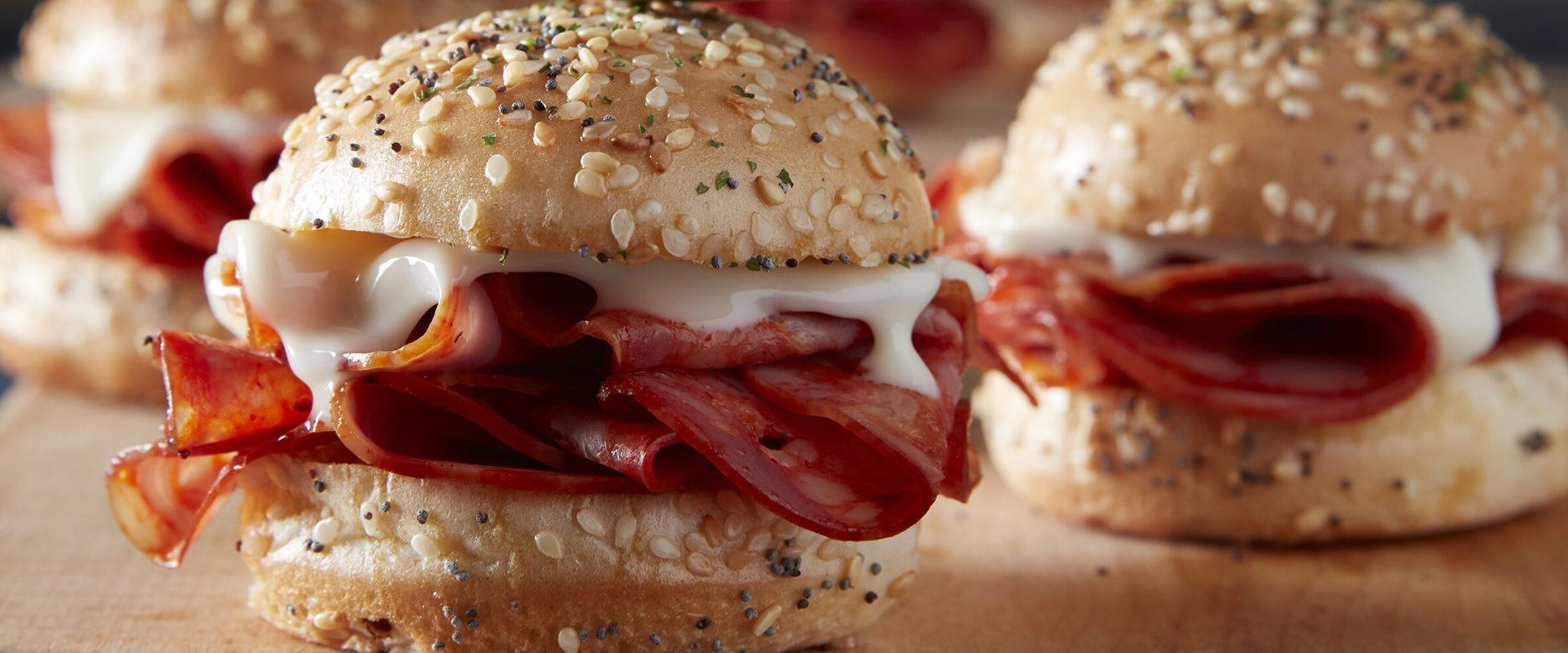 Salami Sliders with melted cheese and a pickle garnish on a cutting board