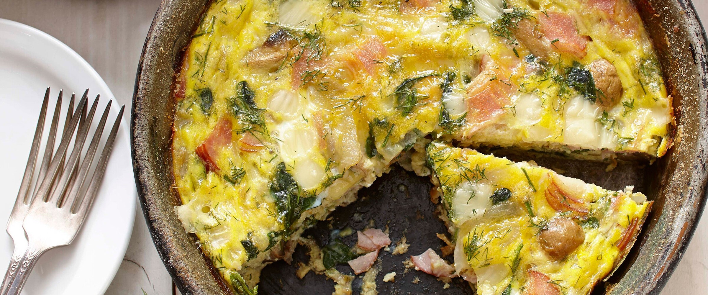 Close-up view of quiche with smoked ham and mushrooms next to white dinner plate.