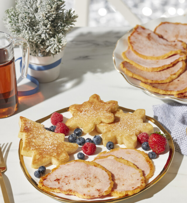 Snowflake and tree shaped pancakes served with berries and peameal bacon on a plate