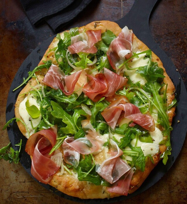 Pizza with arugula and speck prosciutto on a black pan