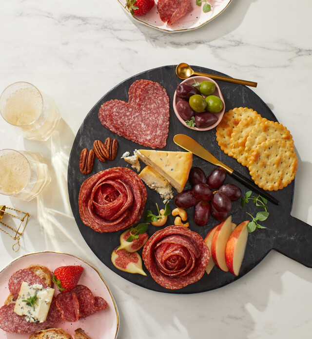 heart shaped salami and flower roses on a black grazing board.