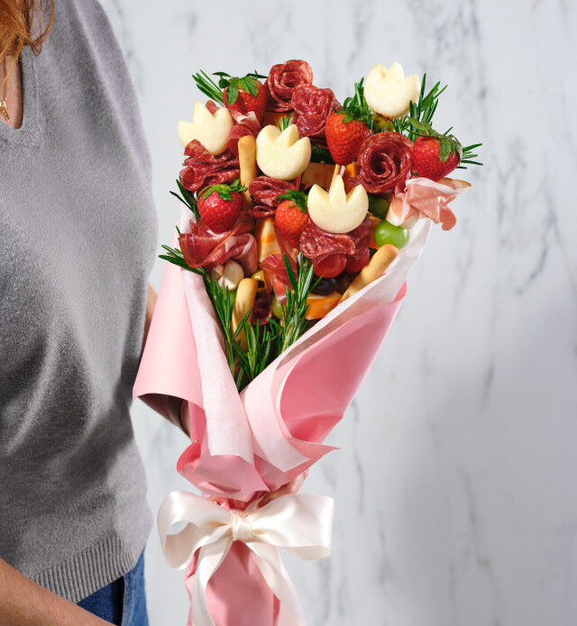 A mix of cheeses, sliced meats and fruits together making a charcuterie bouquet.