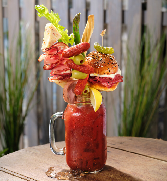 Caesar drink in a mason jar garnished with various veggies and meats.