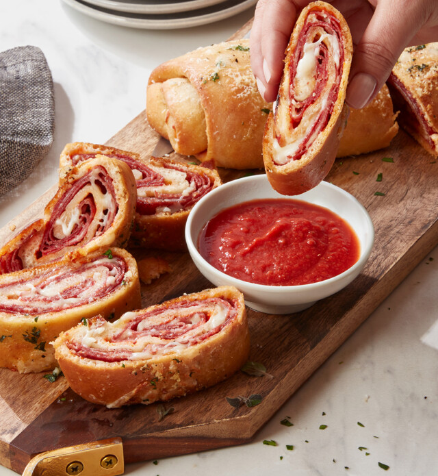 Hand dipping Stromboli into marinara sauce on a wood board