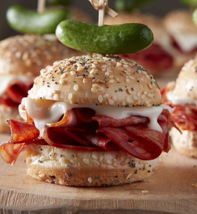 Salami Sliders with melted cheese and a pickle garnish on a cutting board